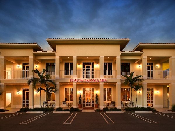 Two-story salon and spa building lit at dusk with palm trees out front