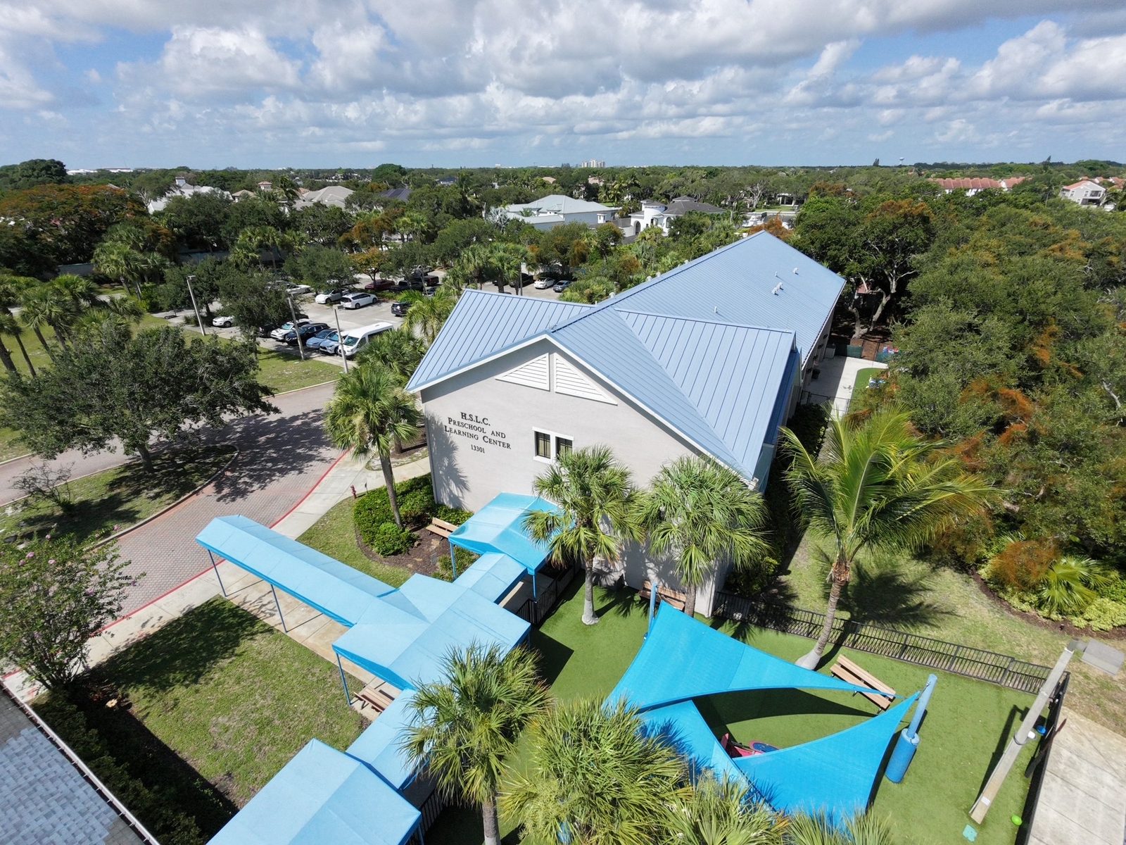 Aerial view of a building with blue shade sails over a playground and courtyard