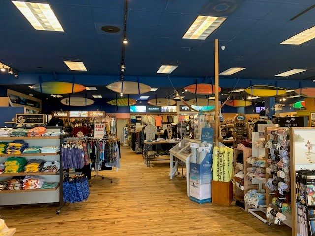 Sales floor with surfboards hung from the ceiling and racks of apparel